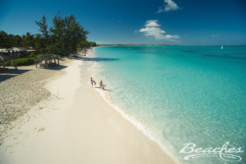 family walking on the beach next to cyrstal clear caribbean waters at beaches turks & caicos