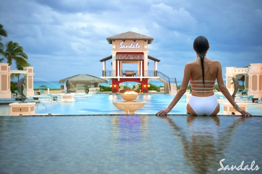 a guest sitting in the pool overlooking the caribbean sea at sandals emerald bay in the bahamas