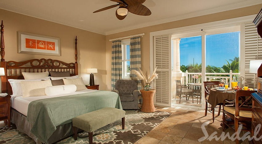 the bed, table and balcony in the beach house luxury club level room at sandals emerald bay