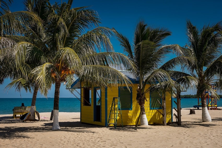 placencia beach with yellow cabin and coconut trees in belize