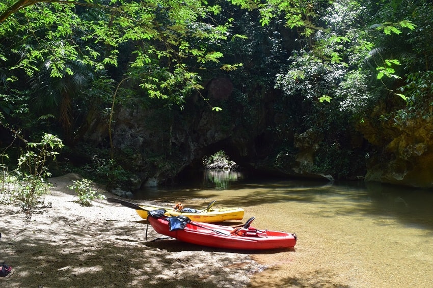 red and yellow kayak on a sandy beach on a river with a jungle and a cave in the background