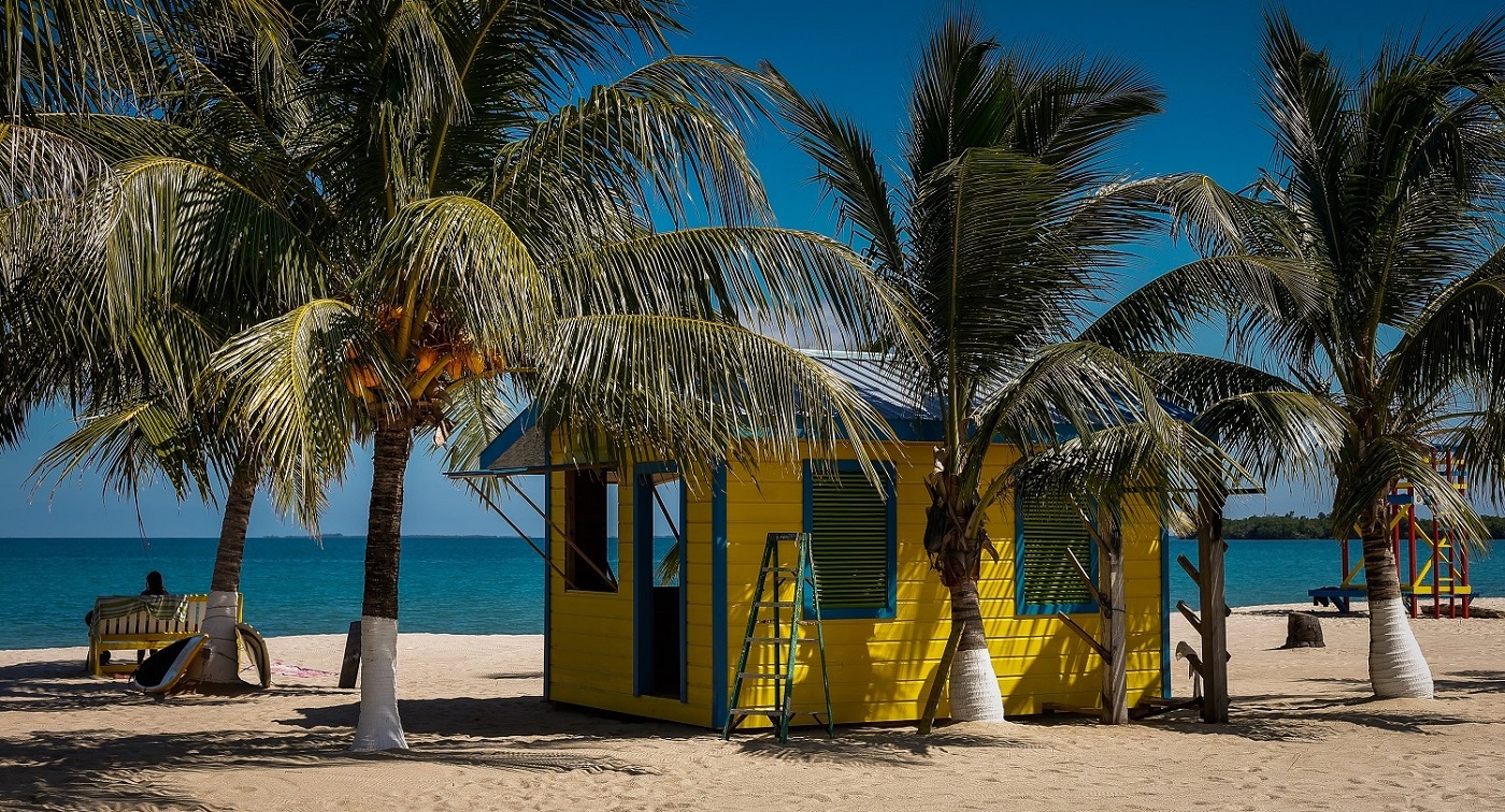 a yellow cabin and guests sitting on the beach in placencia in belize
